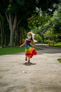 A little girl in a rainbow dress fun running on the concrete path in the park.