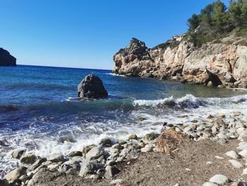 Scenic view of rocks in sea against clear blue sky