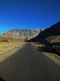 Country road leading towards mountains against blue sky