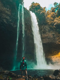 Man standing on rock against waterfall