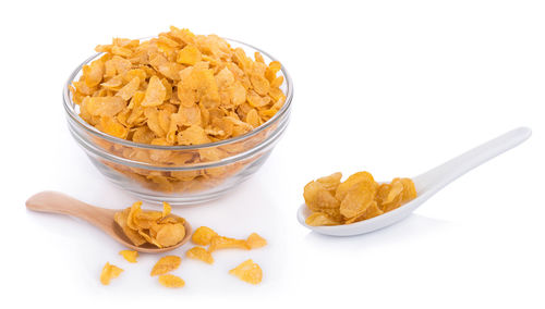 High angle view of corn flakes in bowl and spoons on white background