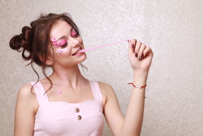 Young woman with pink make-up chewing gum against wall