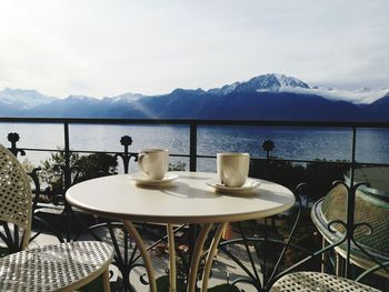 Chairs and table at restaurant by lake against mountains