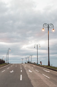 Street lights on road against cloudy sky