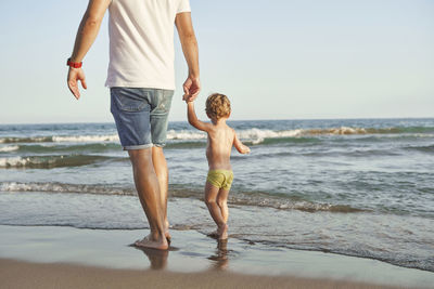 Father and son holding hands while walking at beach