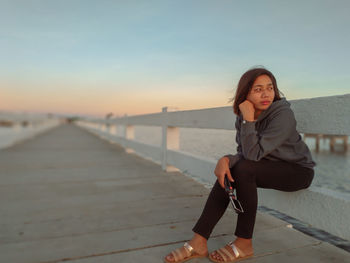 Portrait of young woman sitting against sky during sunset