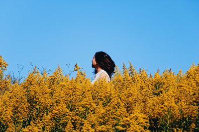 Person standing on yellow flowering plants against sky