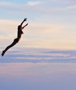 Low angle view of girl jumping against sky during sunset