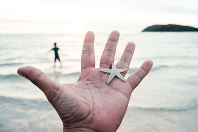 Cropped hand holding starfish over sea against sky