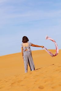 Rear view of woman holding umbrella on beach against sky