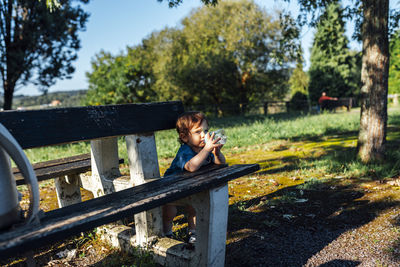 Boy sitting by bench at public park