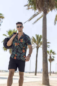 Portrait of young man standing against palm trees