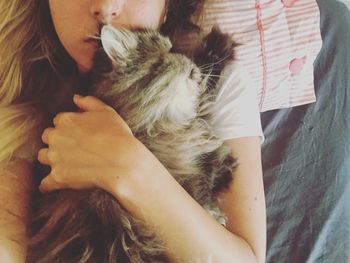 Midsection of woman embracing cat while resting on bed