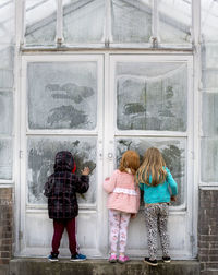 Rear view of girls and boy peeking while standing by closed door during winter