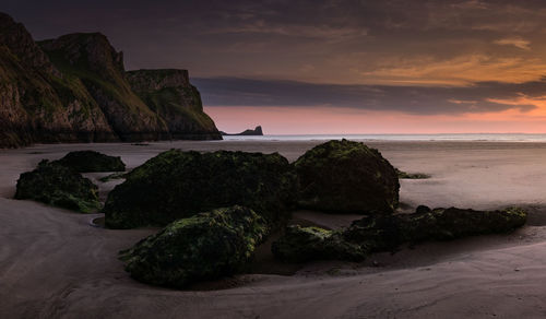 Rock formation on beach against sky during sunset