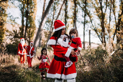 Mother carrying toddler baby while dressed as santa claus in forest