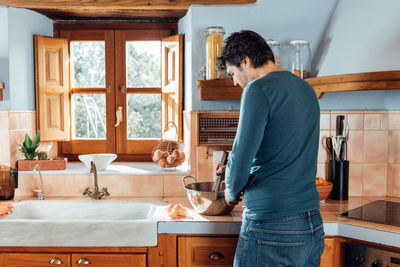 Side view of man looking through window at home