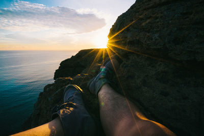 Low section of man on cliff by sea against sky