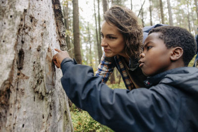 Curious boy pointing at tree trunk by mother in forest during vacation