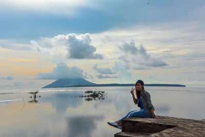 Young woman sitting by sea against sky