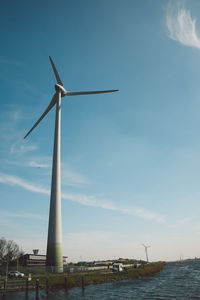 Low angle view of windmill by lake against sky