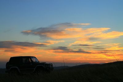 Car on landscape against dramatic sky during sunset