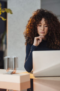 Businesswoman with hand on chin using laptop at desk in office