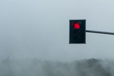 Illuminated road signal against sky during foggy weather