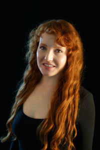 Portrait of smiling young woman against black background