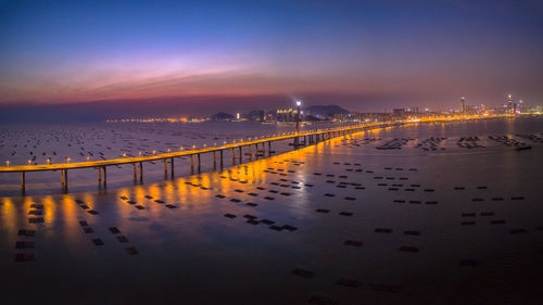 Illuminated city by sea against sky at night