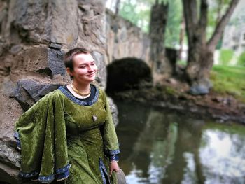 Portrait of smiling young woman standing on rock against trees