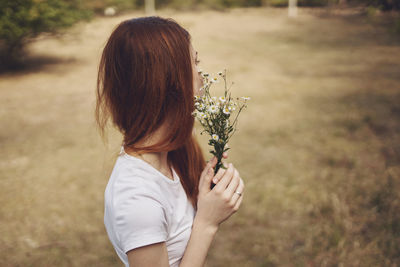 Rear view of woman holding flowering plant on field