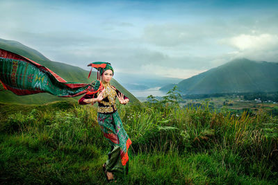 Portrait of woman wearing traditional clothing while dancing on grassy field against sky