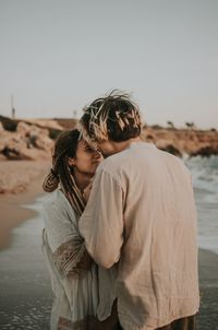 Rear view of couple standing at beach against sky