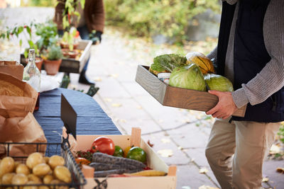 Midsection of man with vegetables container standing at market stall