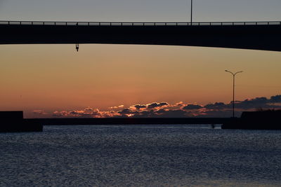 Silhouette bridge over sea against sky during sunset