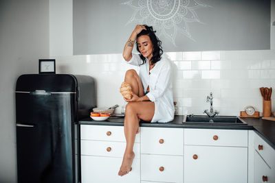 Full length woman holding food sitting at kitchen