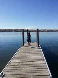 Rear view of woman standing on pier amidst lake