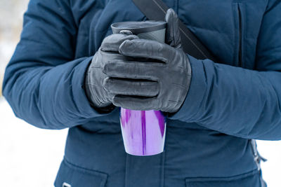 Close-up of the hands of a man holding a purple thermos.