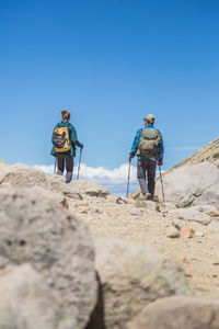 Low angle view of man standing on rock against clear blue sky