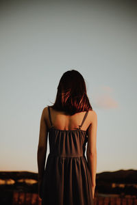 Rear view of young woman standing against clear sky 