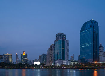 Illuminated buildings in city against clear blue sky