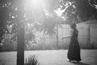 Rear view of woman by tree seen through splashing water in back yard