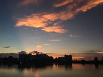 Silhouette buildings by river against sky during sunset