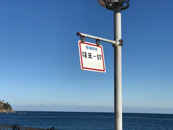 Close-up of sign by sea against clear blue sky