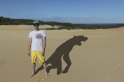Young man standing on beach with wolf shadow