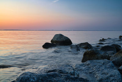 Rocks in sea against sky during sunset