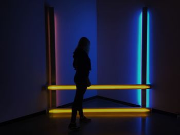 Rear view of woman standing against illuminated wall