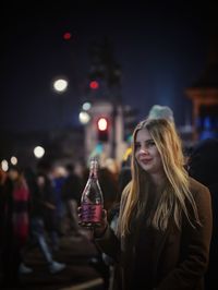 Young woman smiling with drink at night