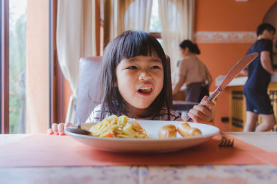 Close-up of girl holding knife while sitting at table in restaurant